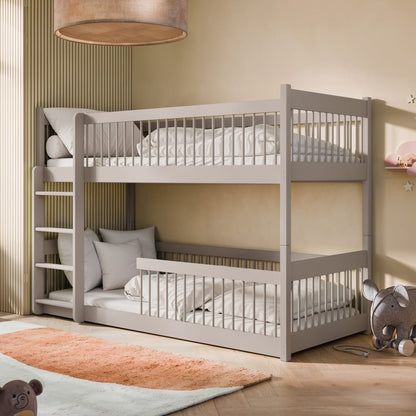 A white wooden bunk bed with a ladder, placed in a room with a light interior. The top bunk is equipped with a guardrail, and there are two beds in total.